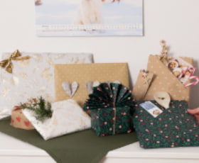 Geschenkverpackungen in verschiedenen Farben und Mustern auf einem Tisch, dekoriert mit etwas Grün.