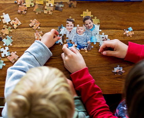 Zwei Kinder setzen gemeinsam ein Puzzle zusammen, auf dem Bilder von ihnen abgebildet sind.