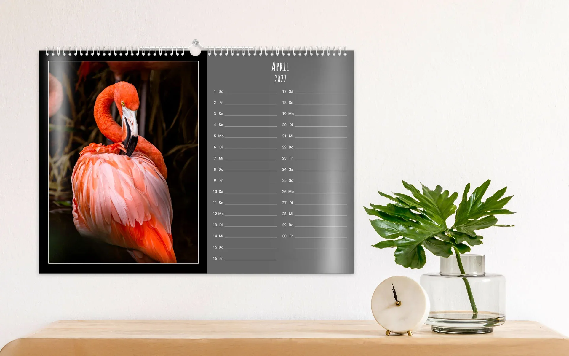 Ein aufgehängter HappyFotokalender ca. A3 quer zeigt ein großes Kalendarium, daneben einen Flamingo vor dunklem Hintergrund.
