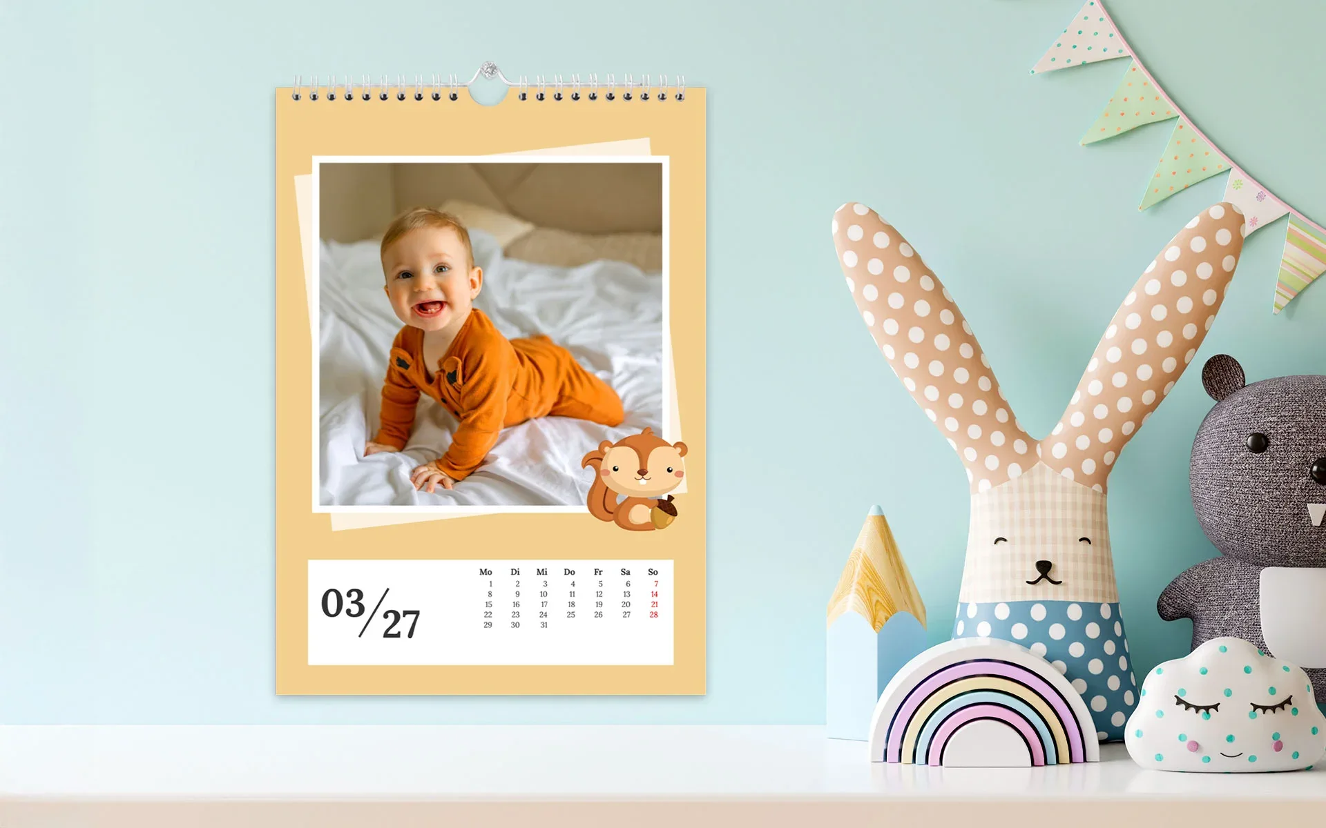 Ein aufgehängter HappyFotokalender ca. A3 hoch zeigt Baby und ein Eichhörnchen Clipart.