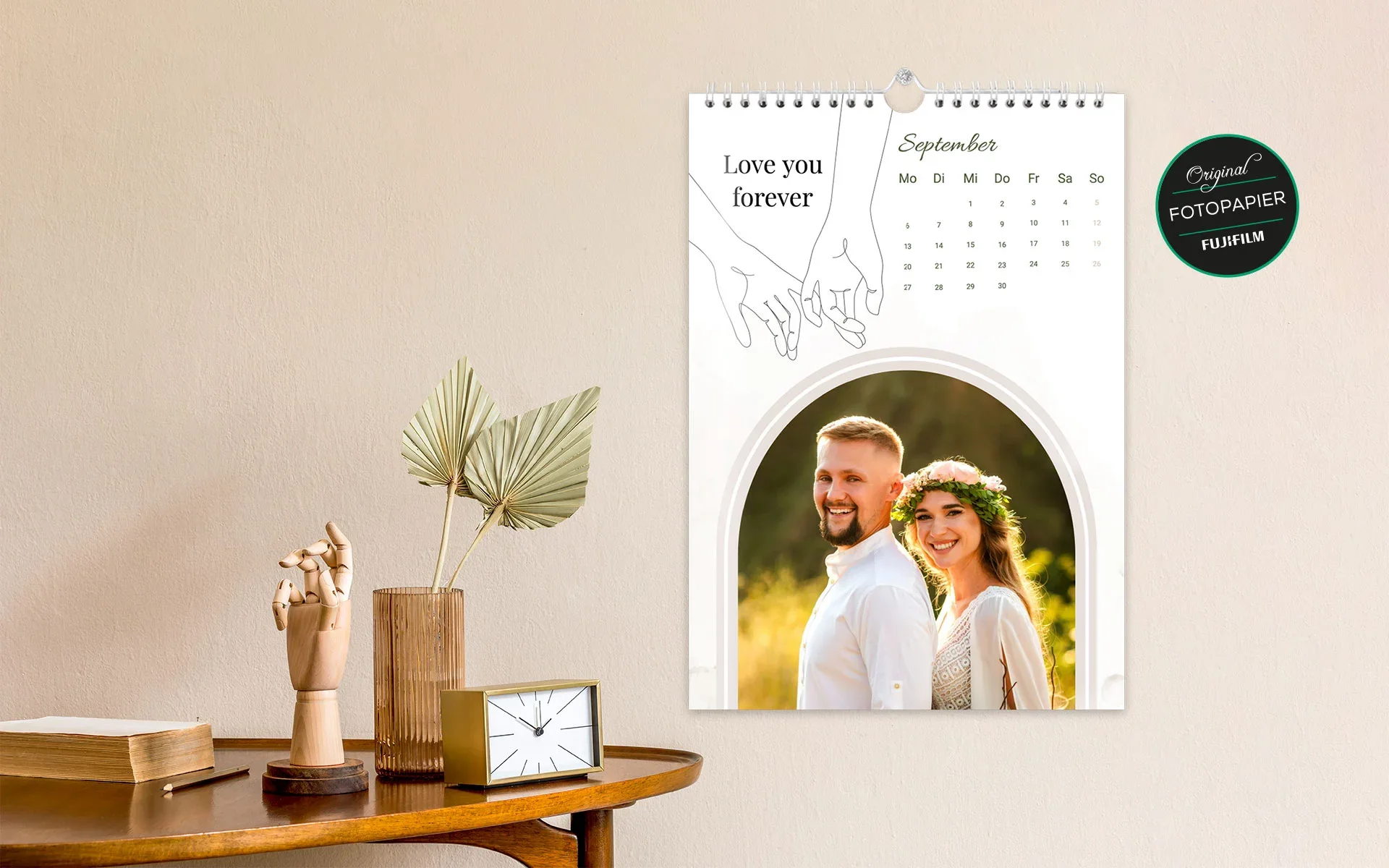 Ein aufgehängter HappyFotokalender ca. A4 hoch mit dem Text Love you forever zeigt ein Brautpaar und ein Hände Clipart.
