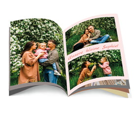 Ein aufgeschlagenes Fotobuch mit Bildern einer Familie im Freien, umgeben von Blumen. Titel: "Unsere kleine Sophie!"
